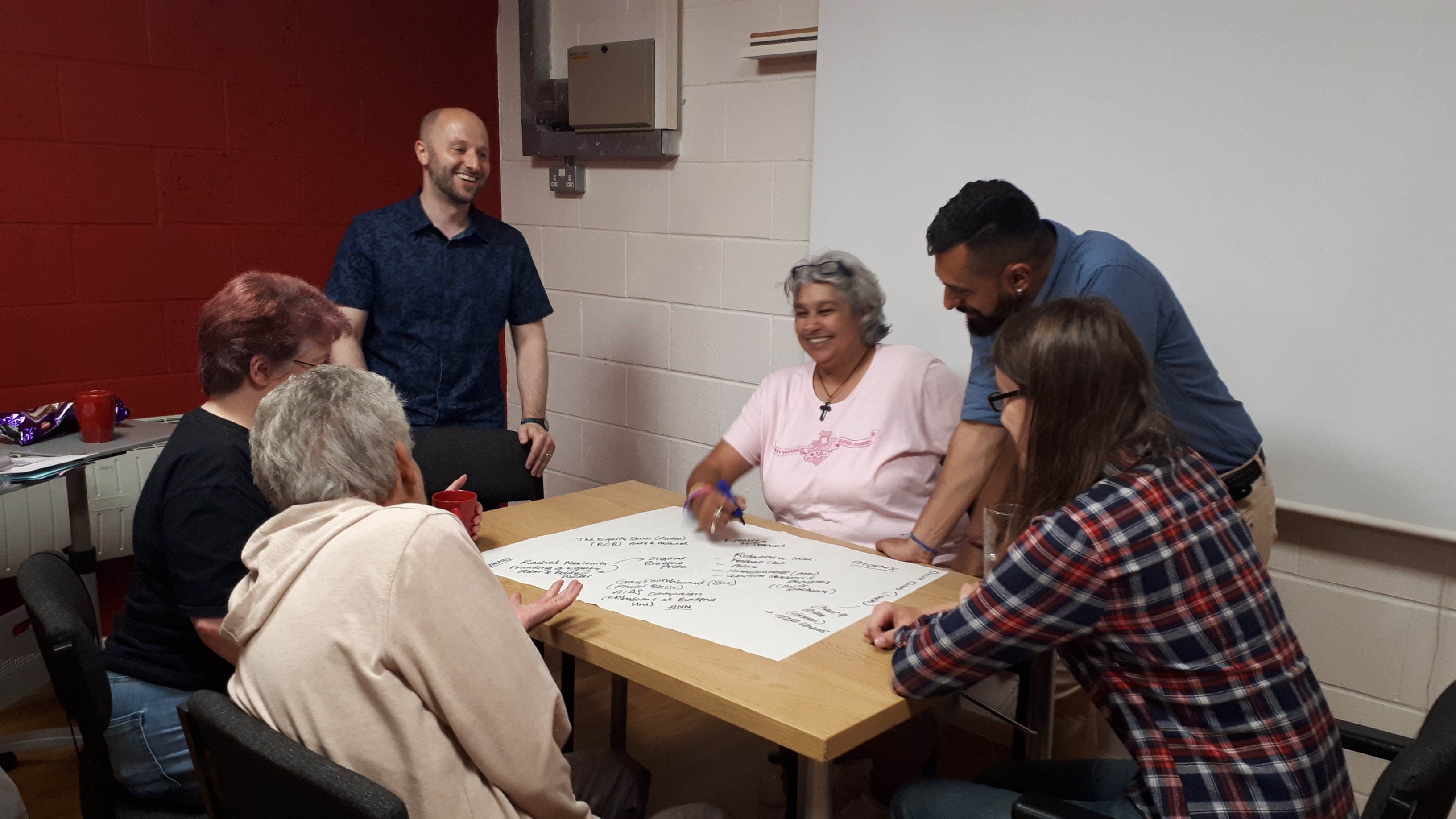 A community group gathers around a table writing on flip chart paper.