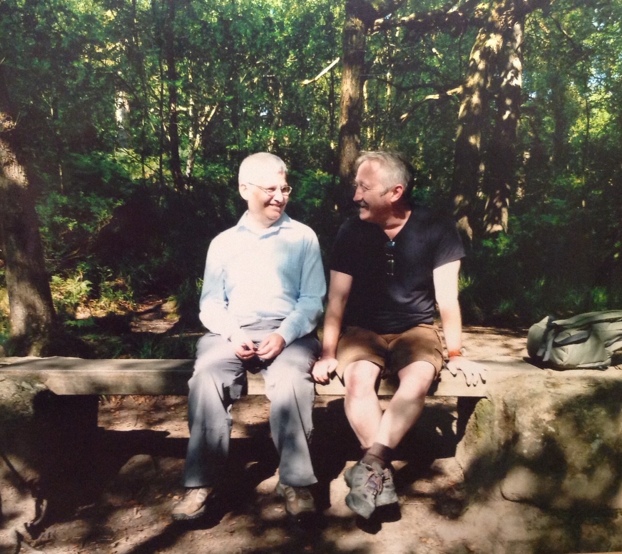 David and his partner Aram sit on a wooden bench in the woods